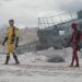 Image of Wolverine walking away from Deadpool in a barren landscape. There is part of a ship behind them.
